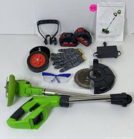 Photo of all contents including cordless trimmer with metal shaft, two 21V batteries, charger, circular cutting blade, plastic guard, detachable handle, wheels, gloves, safety glasses, and instruction manual.