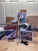 Photo showing cordless handheld vacuum cleaner, mattress vacuum bag box, adjustable lamp, immersion water heater box, garment iron, and bidet sprayer set.