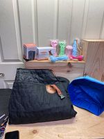 Black quilted dog car seat cover folded on table with boxed devices and plastic toys on wooden shelf behind