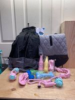 Full view of black rain jacket, grey quilted dog jacket, blue anti-bark collar box, and assorted dog toys including knotted ropes and bottle-shaped chew toys.