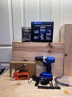 Lot arranged on wooden blocks with all items visible including drill, staple tool, boxed cordless wood trimmer, oscilloscope, drill bits and charger.
