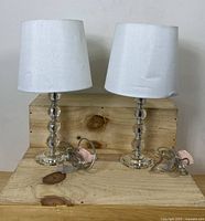 Two European-style crystal table lamps with white shades on a wooden surface, front view.