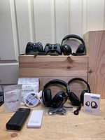 Full lot including gaming controllers on top row and over-ear headphones, earbuds, power banks, and TV RGB lighting strips on wooden platform.