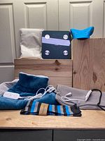 All items arranged on wooden surface with grounding sheet in background, scale centered, heating pad and cover with cables, socks in front, and neck massager on the right.