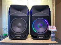 Front view of two ION PA Extreme speakers, one with LED lights off and the other illuminated with multi-colored LED ring around the woofer.