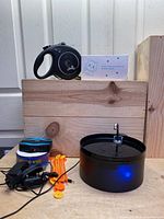 Photo showing black retractable pet leash, automatic pet water fountain, and pet fencing system components including wire, stakes, and power adapter