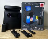 Photo of RCA projector, two microphones, remote control, power adapter, and original packaging box showing device and features.
