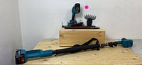 Full view of cordless tool setup on a wooden box and extendable pole laid flat showing tool handle, pole, and attachments in background.