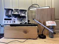 Photo showing the assembled desk clamp LED light with a slim rectangular LED bar and the tubular LED light fixture placed in front. A sign notes items are untested.