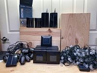 Entire lot showing various solar lights including multiple animal repellers, stakes for solar lights, solar string lights, solar paneled solar powered lights and lantern style lights on wooden stand.