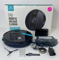 Deenkee D40 boxed robotic vacuum with several included accessories such as water tank, charger, side brushes, filter, and cleaning accessories arranged in front.
