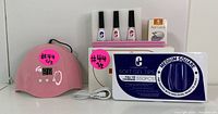 Photo showing pink UV LED lamp, three bottles of gel polish, nail file, buffer, and box of soft gel nail tips.