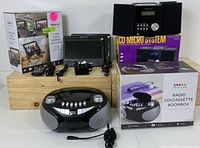 Photo shows a Proscan box for a CD Micro System, a CD/Cassette Boombox with box, a portable screen with remote and power cables, and various accessories displayed on a wooden surface.