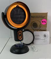 Front view of the NI portable desktop heater turned on, showing orange heater element, control buttons, water tank, user guide, filter, and packaging box