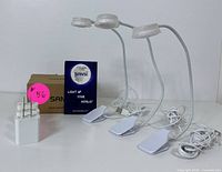 Three white LED clip-on desk lamps with flexible gooseneck arms shown with a USB power adapter, cardboard box, and instruction manual.