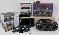 Photo showing the complete entertainment bundle including packaged dual screen DVD player, remote, power cables, DVD player in box, and Bluetooth boombox in original packaging.