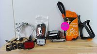 Full overview of bicycle accessories on wooden surface showing LED front and rear lights, multi-tool repair kit, water bottle holder, reflectors, and pedal clips.