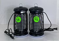 Photo of two black electric bug zappers with hanging hooks and power cords shown side-by-side.