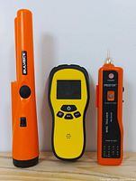 Photo of three detection tools showing front view of Bulvack pinpointer metal detector, yellow wire tracer device with screen and buttons, and orange PROSTER wire tracker with power and test buttons.