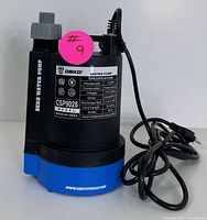 Front and side view of the Deko CSP9028 submersible water pump showing label with specifications and power cord coiled beside it.