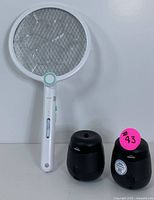 Photo of a white rechargeable electric mosquito swatter with circular metal electric grid and two Thermacell black repellent units side by side.