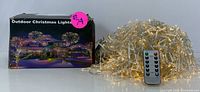 Outdoor Christmas string lights and remote control with original packaging showing festive house lighting examples.