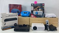 Photo showing the entire lot with projector, DVD player, Bluetooth boombox, speakers, remotes, cables and fabric accessories