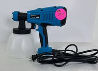 Blue and black Tilswall electric paint sprayer showing front side with white plastic paint container and power cord coiled beside.