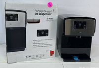 Photo showing sealed box alongside the portable nugget ice dispenser unit with product details visible on box.