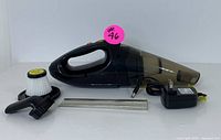 Cordless handheld vacuum cleaner with dust container, attachments including crevice tool, brush nozzle, extra filter, and charger power adapter, laid out on white background.