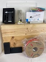 Photo showing the 3D printing pen packaging, the pen itself alongside accessories including charging cables, two power banks, and a coil of filament in plastic wrap placed on a wooden surface.