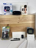 Full view of all items in lot including blood pressure monitor box, smart watch box, bicycle computer in package, smart band, and blood pressure monitor cuff and unit.