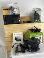 Full lot image showing all included items on a wooden surface: MP5 player, TPMS tool, MagSafe mount box, garage remote, and electric air pump with accessories.