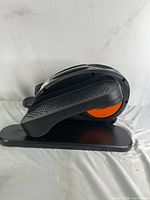 Side view of the compact elliptical machine showing black and orange foot pedals and base.
