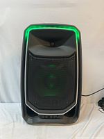 Front view of ION PA Freedom speaker showing black grille, woofer and tweeter behind grille, green LED edge-glow lights active.