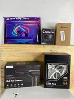 Full lot overview including boxes of LED neon rope lights, webcam, power strip, K2 Air Duster and ARGB case fan on wooden shelf.