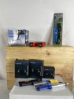 All items displayed on wooden box: LED headlight boxes, red flashlights, soldering iron in packaging, voltage detector pen, desoldering pump.