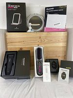 Full lot shows all items including trimmer, hair straightener brush, two smart watches, and two makeup mirrors in boxes and unpacked.