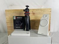 Lot items arranged on wooden board: Monster Ear Buds box and earbuds case, Mobifoto tripod, Neewer LED light, white power bank, and wireless charger.