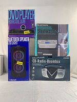 Boxed set of four electronic audio and video devices stacked: Progressive Scan DVD Player, Bluetooth Speaker with LED Light, Sylvania Bluetooth Under Counter CD Clock Radio, Retro Portable CD Radio Boombox.