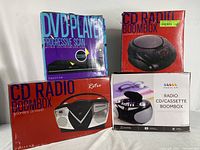 Photo of four boxed items: two Proscan CD Radio Boombox units, one retro style and one compact, plus a Proscan DVD player and an additional CD Radio Boombox.