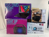 Lot with boxed 15.6 DVD portable player, light up Bluetooth speaker, portable Bluetooth boombox, and RCA home theater projector in white