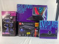 Full set of the four boxed items including RCA projector with 100" screen, Sylvania Bluetooth speaker, 15.6" portable DVD player, and progressive scan DVD player.