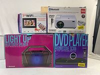 Overview of boxed items including RCA home theatre projector, 7-inch WiFi digital photo frame, progressive scan DVD player, and light-up Bluetooth speaker.