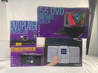 Photo showing all three boxed items together: Portable DVD Player (purple box), DVD Player Progressive Scan (yellow box), and CD Micro System Digital Radio (black box)