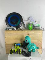 Photo showing the lot with LED frisbee, gel blaster, remote control car with controller, and dinosaur toy on wooden surface.