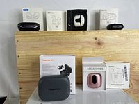 Full lot of five models of true wireless earbuds, their charging cases, boxes, and manuals arranged on wooden platform.