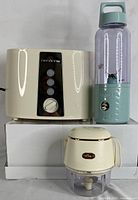 Photo showing all three items: cream 2-slot toaster, purple and teal portable blender, and cream baby food processor with gold band.