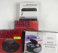 Four Proscan electronic devices showing retail boxes with product images and labels: HDMI Upconvert DVD player, Cassette CD AM/FM Radio, CD Radio Boombox, and Radio CD/Cassette Boombox.