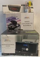 Boxes of Sylvania clock radio, Proscan radio CD/cassette boombox, and Proscan Bluetooth CD micro system stacked